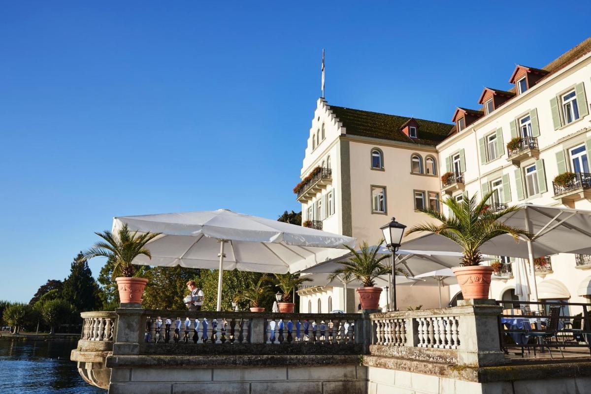 ein Restaurant mit Tischen und Sonnenschirmen vor einem Gebäude in der Unterkunft Steigenberger Inselhotel in Konstanz