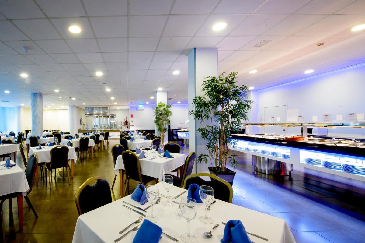 un restaurante con mesas blancas y sillas con servilletas azules en Hotel Bonalba Alicante, en El Campello
