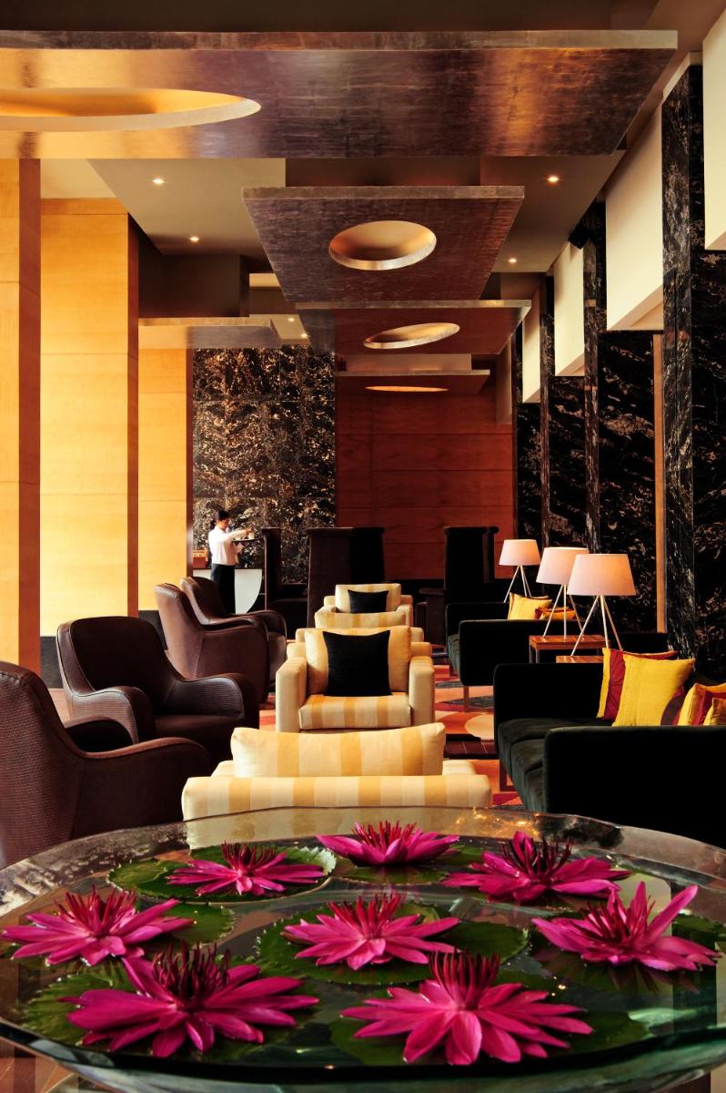 a lobby with chairs and a table with flowers on it at Taj Club House in Chennai a lobby with chairs and a table with flowers on it at Taj Club House in Chennai