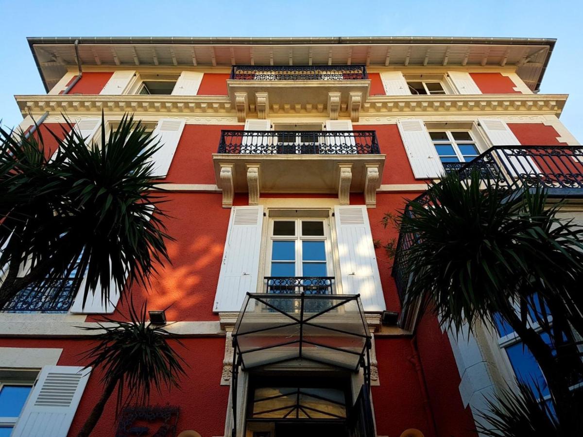 un grand bâtiment rouge avec des palmiers devant dans l'établissement Hôtel & Espace Bien-être La Maison du Lierre, à Biarritz