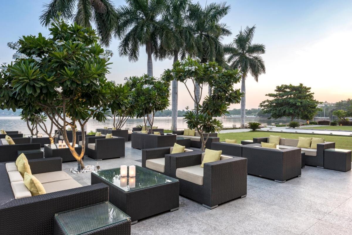 a patio with couches and tables and palm trees at Hotel Lakend in Udaipur