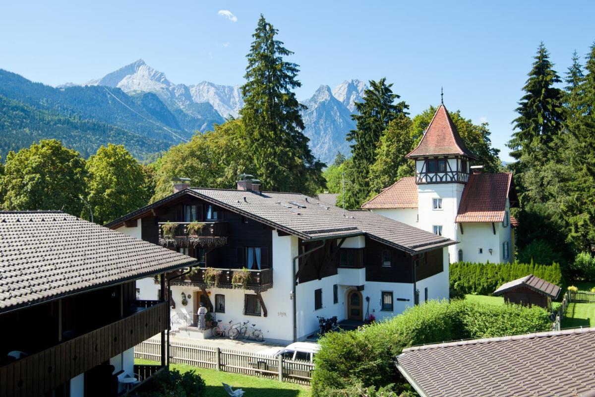 ein großes weißes Haus mit einem Turm und Bergen in der Unterkunft HYPERION Hotel Garmisch - Partenkirchen in Garmisch-Partenkirchen ein großes weißes Haus mit einem Turm und Bergen in der Unterkunft HYPERION Hotel Garmisch - Partenkirchen in Garmisch-Partenkirchen