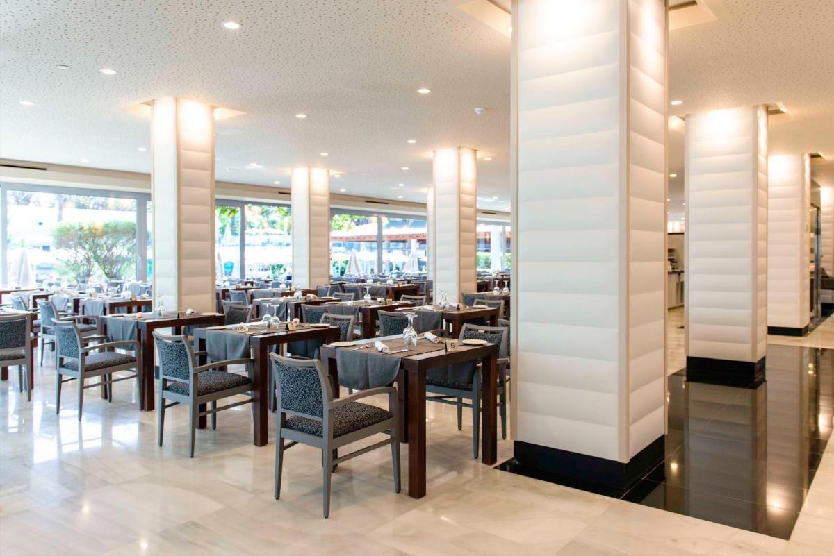 Un comedor con mesas y sillas y ventanas. en Spring Hotel Vulcano, en Playa de las Américas