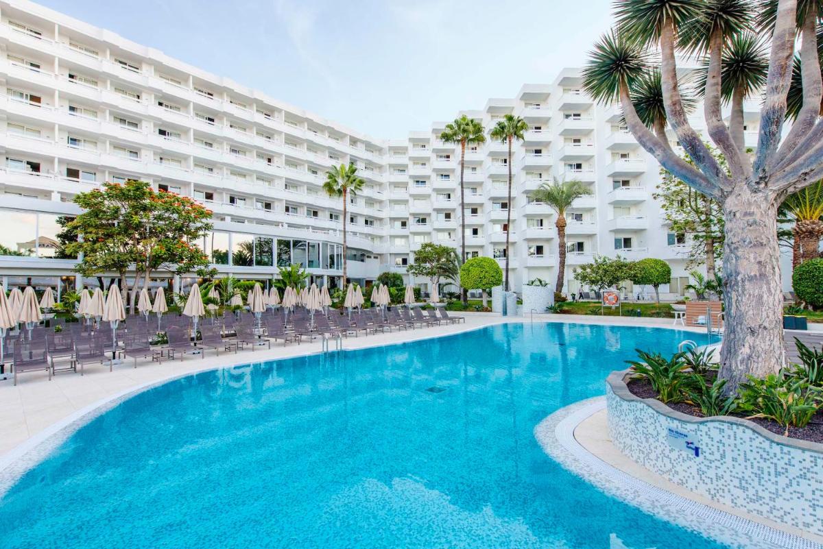 Una piscina con sillas y un gran edificio. en Spring Hotel Vulcano, en Playa de las Américas