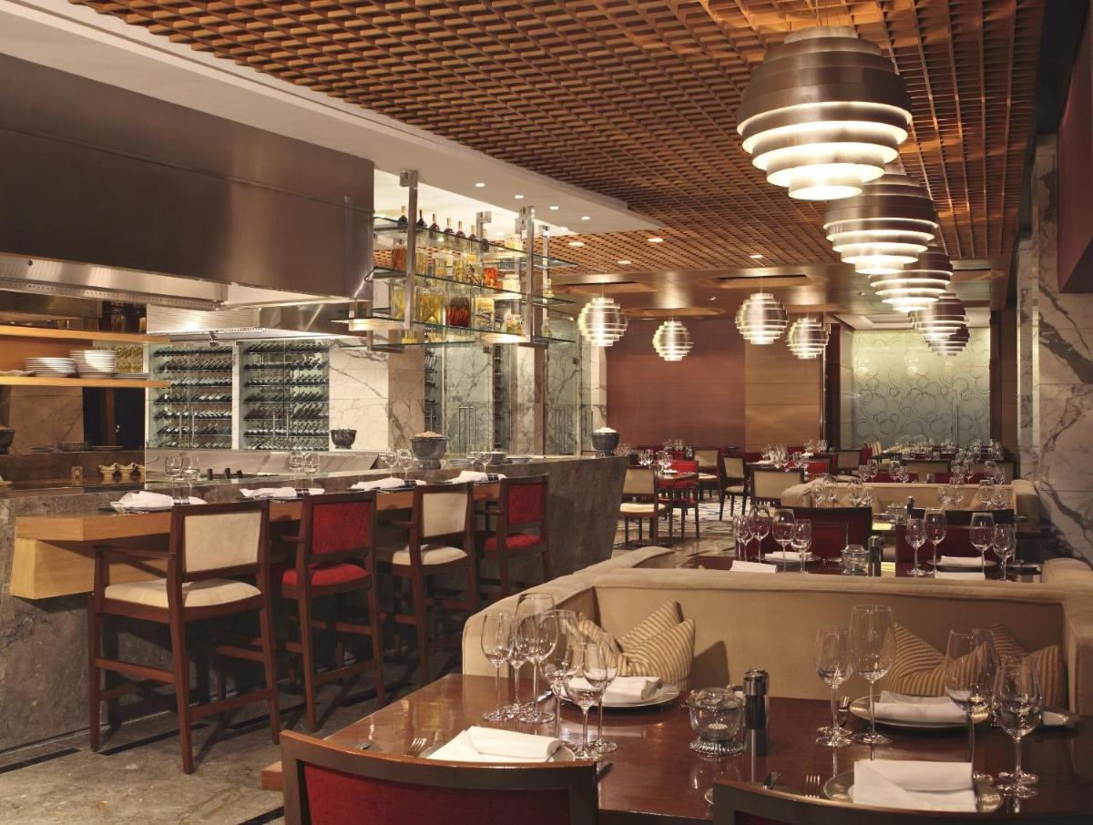 a restaurant with tables and chairs and a bar at The Leela Ambience Gurugram Hotel & Residences - The Luxury Urban Sanctuary in Gurgaon