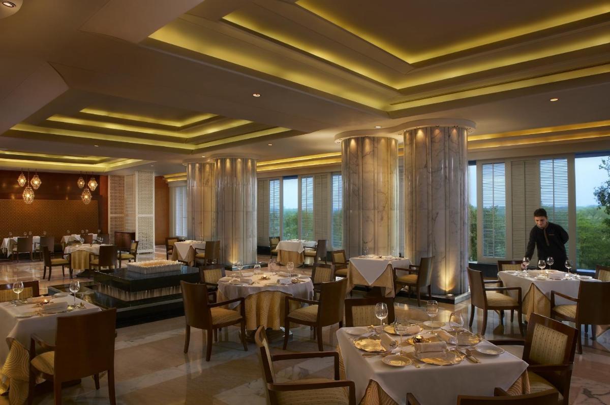a restaurant with tables and chairs and a man standing in the middle at The Leela Ambience Gurugram Hotel & Residences - The Luxury Urban Sanctuary in Gurgaon