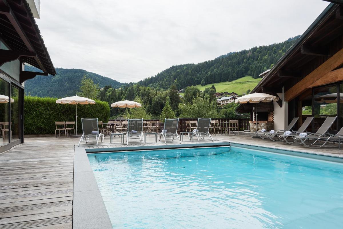 une piscine avec chaises et parasols sur un bâtiment dans l'établissement Hotel le Petit Dru, à Morzine