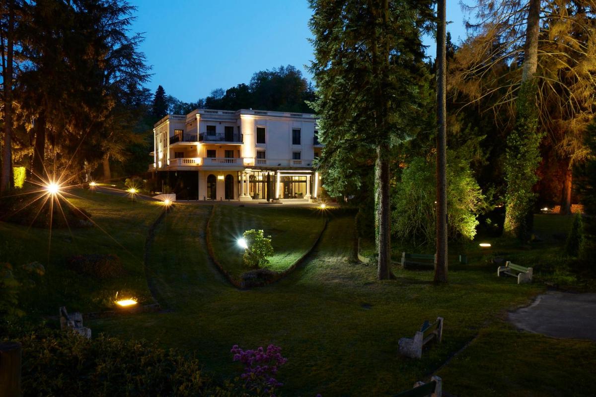 une grande maison blanche avec des lumières sur la pelouse dans l'établissement Hotel & Spa Le Pavillon, à Charbonnières-les-Bains
