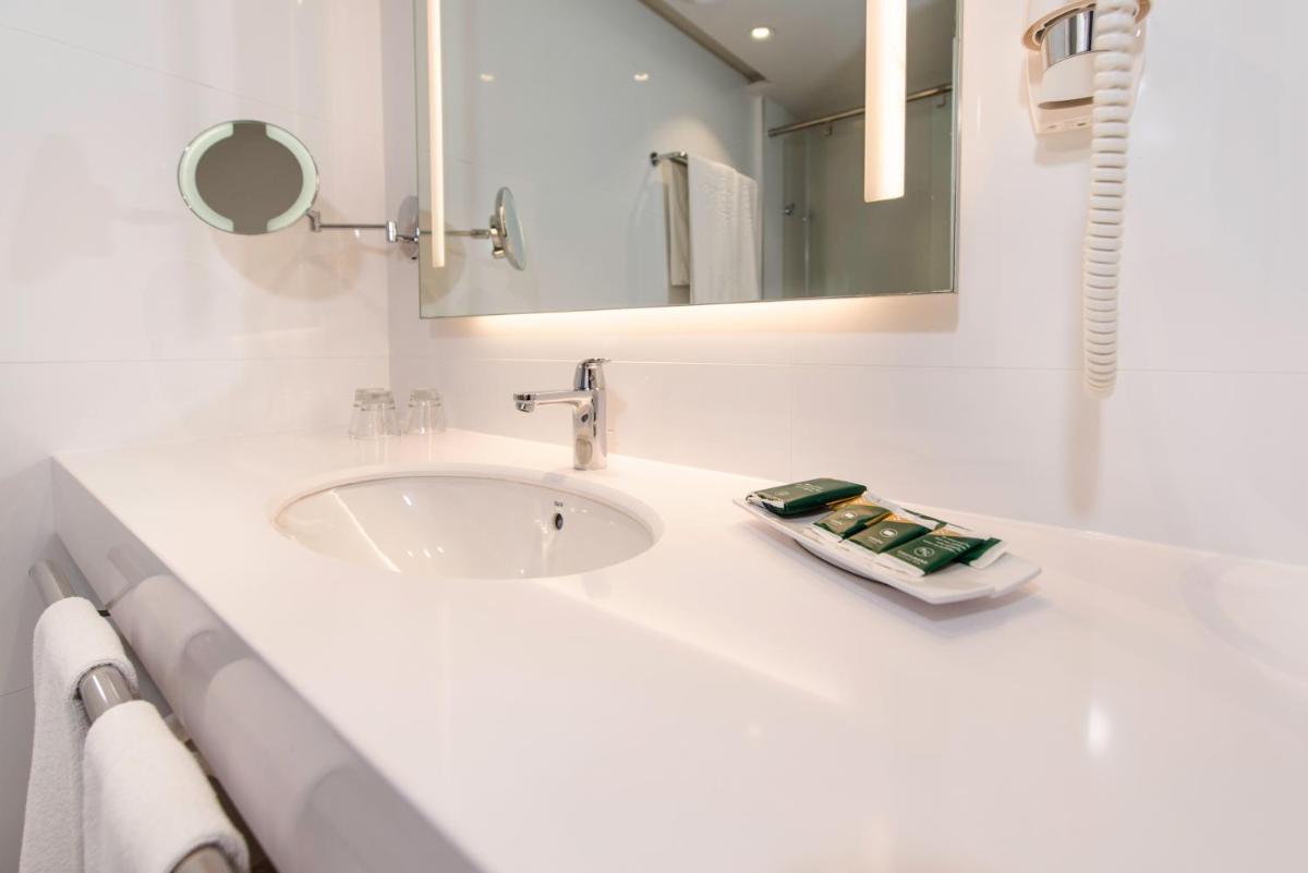 Un baño blanco con lavabo y espejo. en Spring Hotel Vulcano, en Playa de las Américas