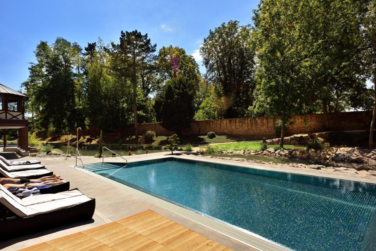 - une piscine dans une cour avec 2 chaises longues dans l'établissement Hotel Spa Restaurant Domaine du Moulin, à Ensisheim