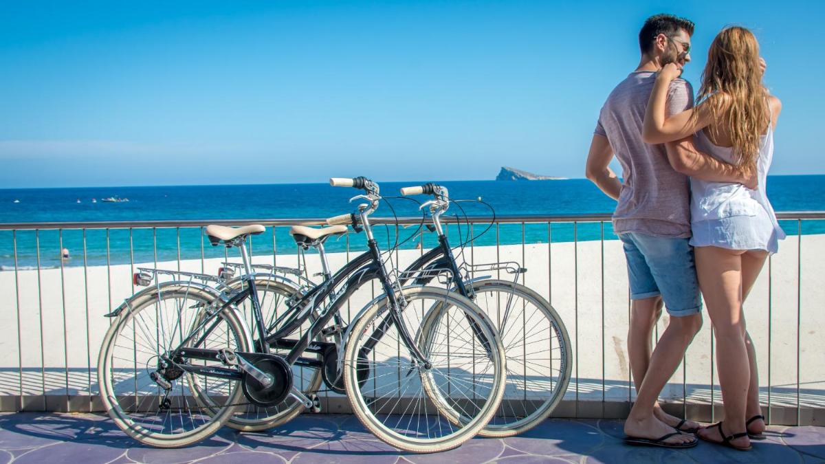 Dos mujeres de pie junto a una bicicleta al lado de la playa. en Hotel RH Victoria & Spa 4 Sup, en Benidorm
