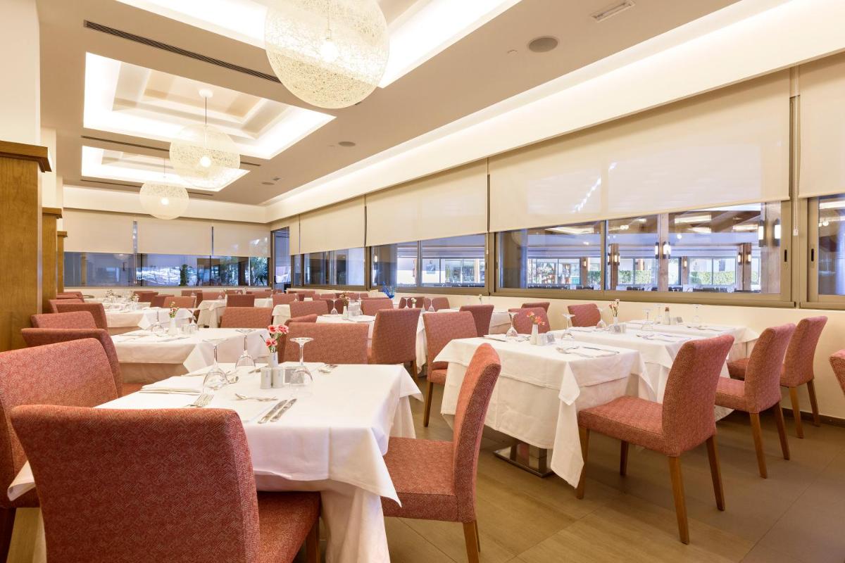 Un restaurante con mesas y sillas blancas y ventanas. en Hipotels Cala Millor Park, en Cala Millor