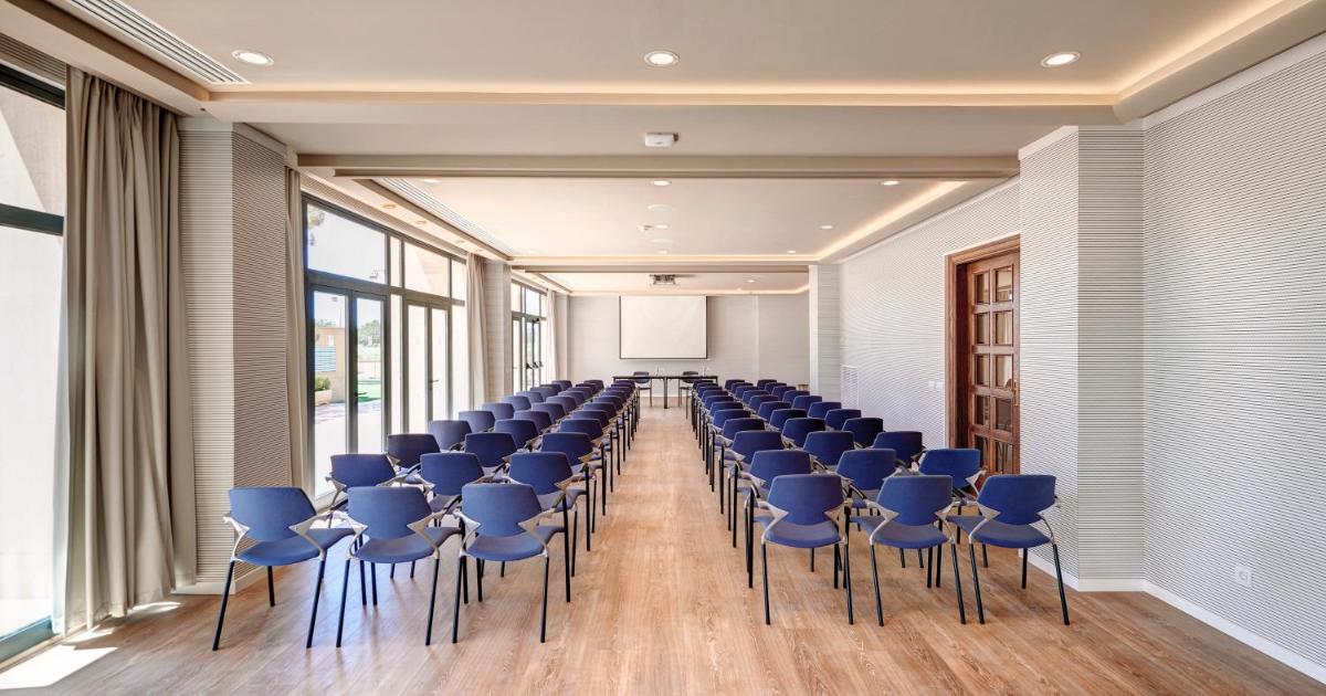 una sala de conferencias con sillas azules y una pantalla en Hipotels Hipocampo Palace & Spa, en Cala Millor