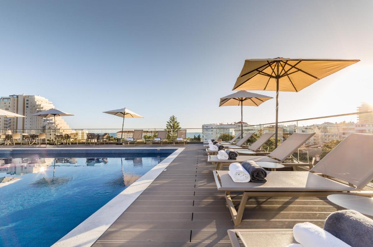 uma piscina de hotel com espreguiçadeiras e guarda-sóis em The Prime Energize Hotel & SPA - Algarve em Monte Gordo