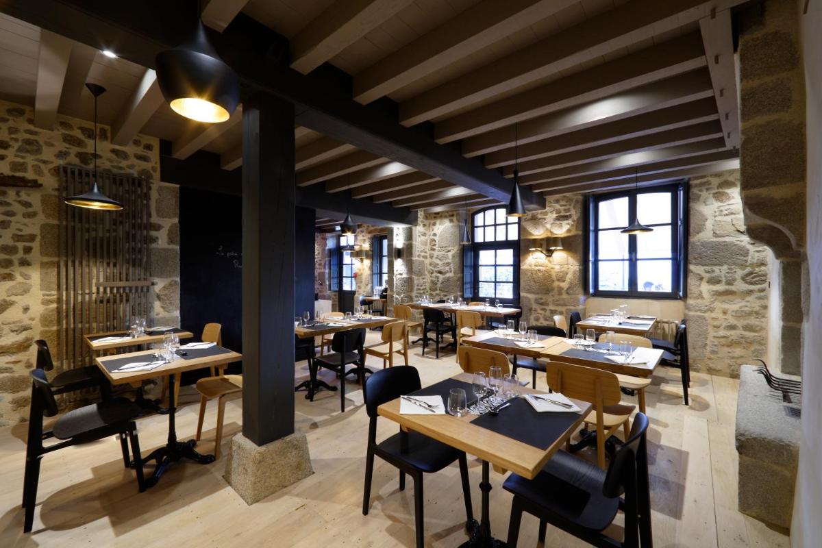un restaurant avec des tables et des chaises en bois et des murs en pierre dans l'établissement Les Maisons du Pont - Charme & Caractère, à Aubusson