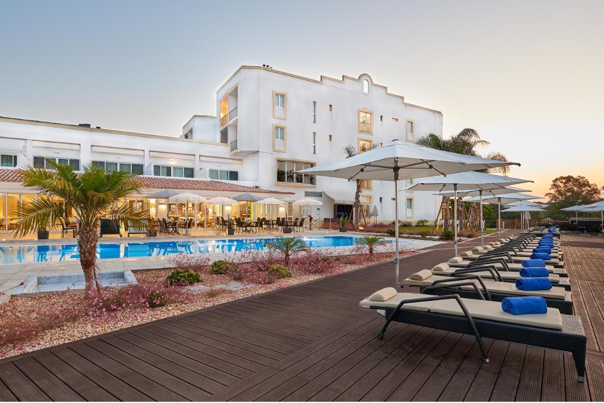 um hotel com espreguiçadeiras e guarda-sóis ao lado de uma piscina em Dona Filipa Hotel no Vale do Lobo