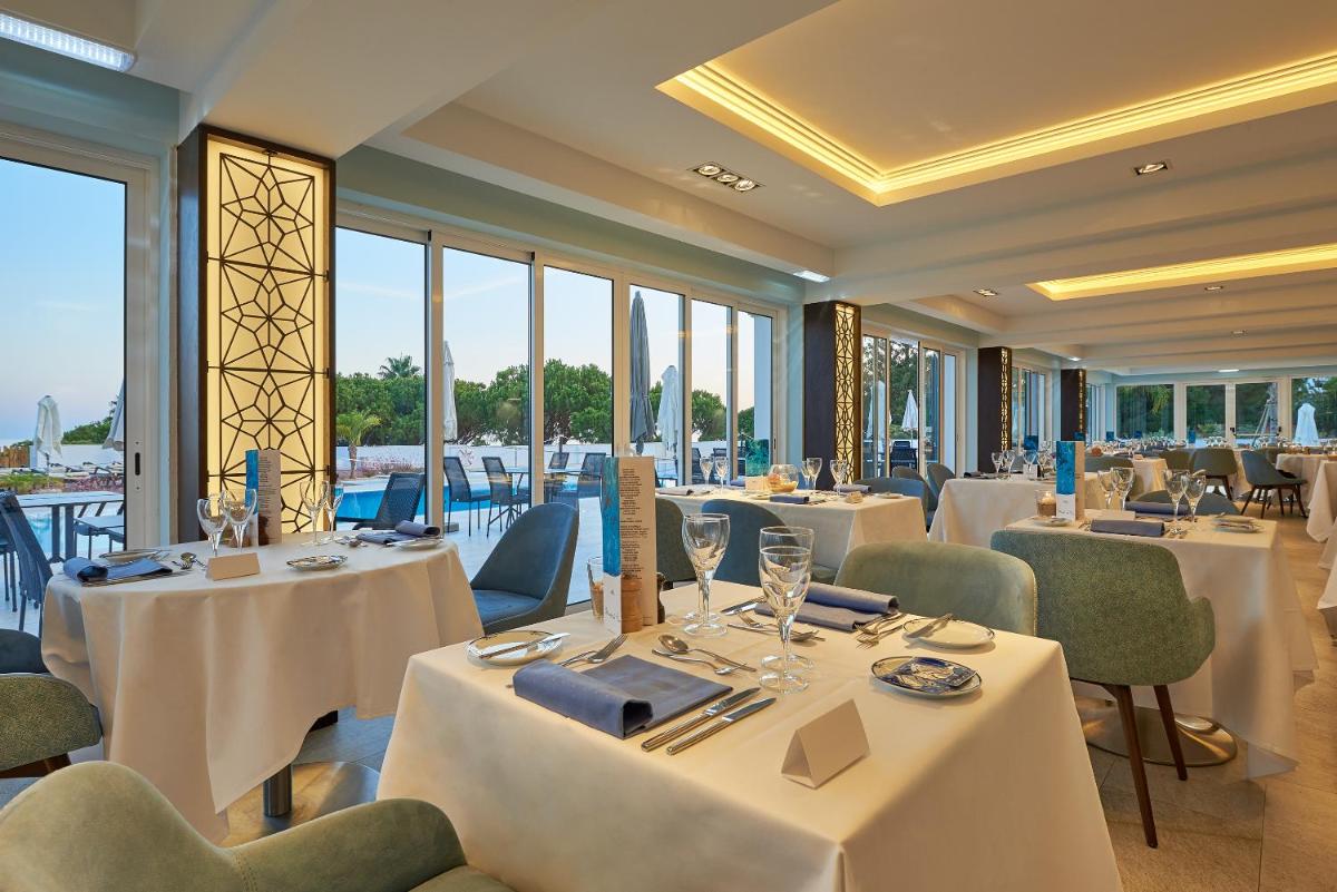 um restaurante com mesas, cadeiras e janelas brancas em Dona Filipa Hotel no Vale do Lobo