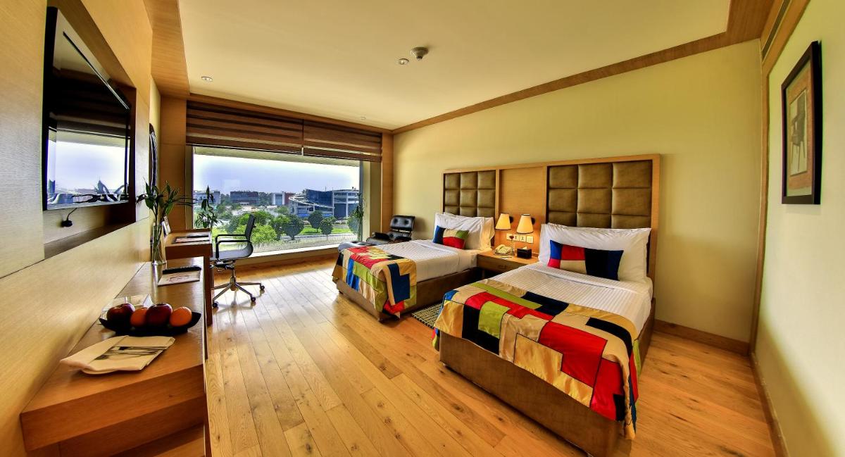 a bedroom with two beds and a desk and a window at The Lalit Chandigarh in Chandīgarh