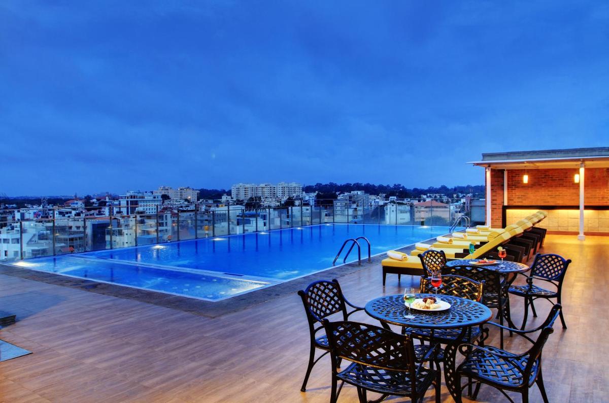 a balcony with tables and chairs and a swimming pool at Hotel Royal Orchid Bangalore in Bengaluru a balcony with tables and chairs and a swimming pool at Hotel Royal Orchid Bangalore in Bengaluru