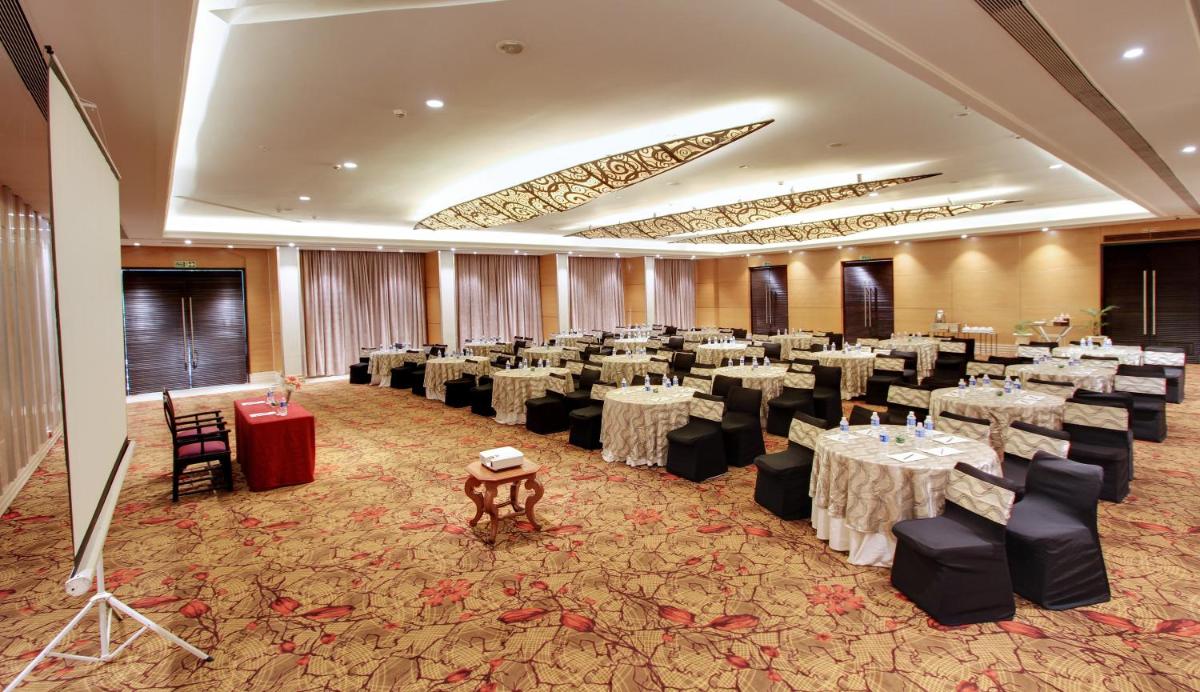 a banquet hall with white tables and black chairs at Hotel Royal Orchid Bangalore in Bengaluru