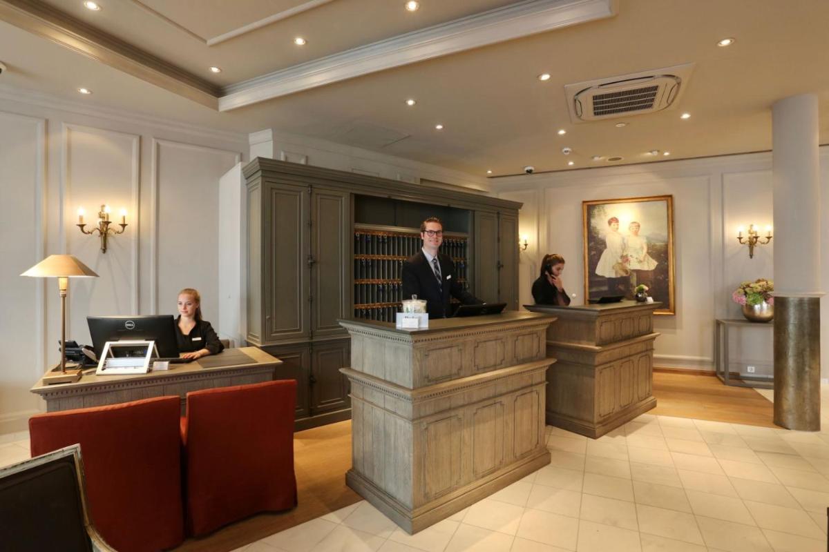 3 Personen sitzen an der Rezeption in einer Lobby in der Unterkunft Hotel München Palace in München 3 Personen sitzen an der Rezeption in einer Lobby in der Unterkunft Hotel München Palace in München