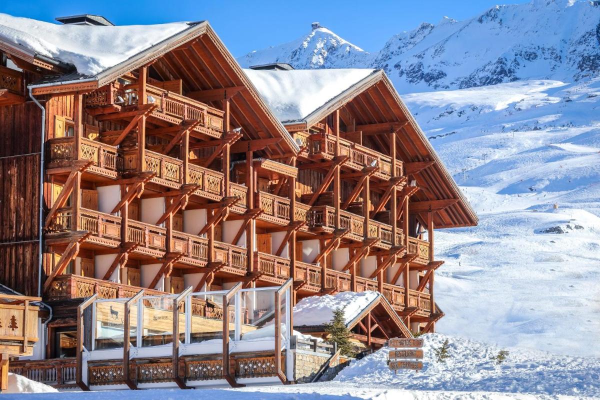 un grand bâtiment en bois dans la neige avec des montagnes dans l'établissement Hôtel Au Chamois d'Or by Les Etincelles, à L'Alpe-d'Huez
