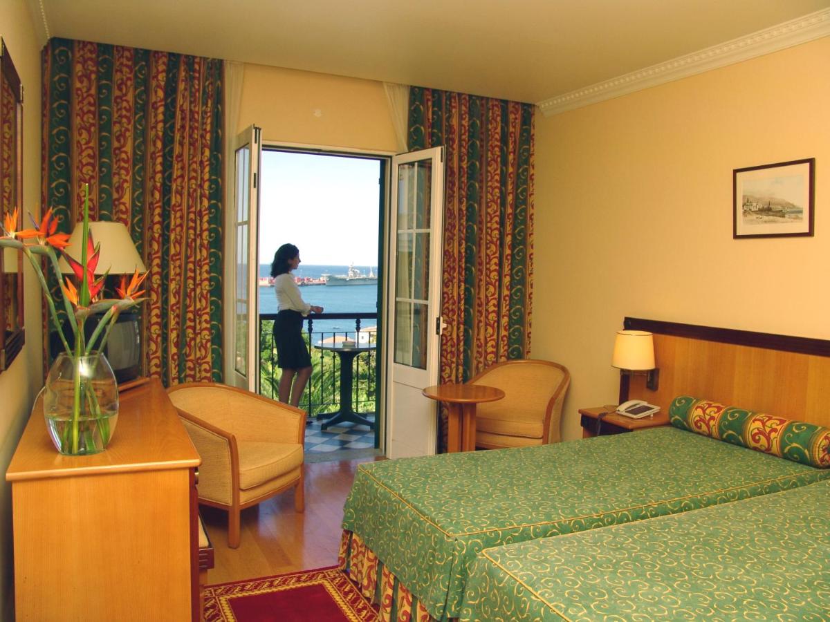 um quarto de hotel com uma mulher a olhar pela janela em Hotel Quinta Bela S Tiago no Funchal