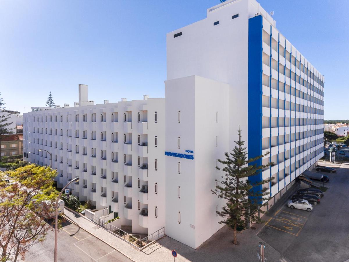 um prédio branco com uma árvore na frente em Hotel Navegadores em Monte Gordo