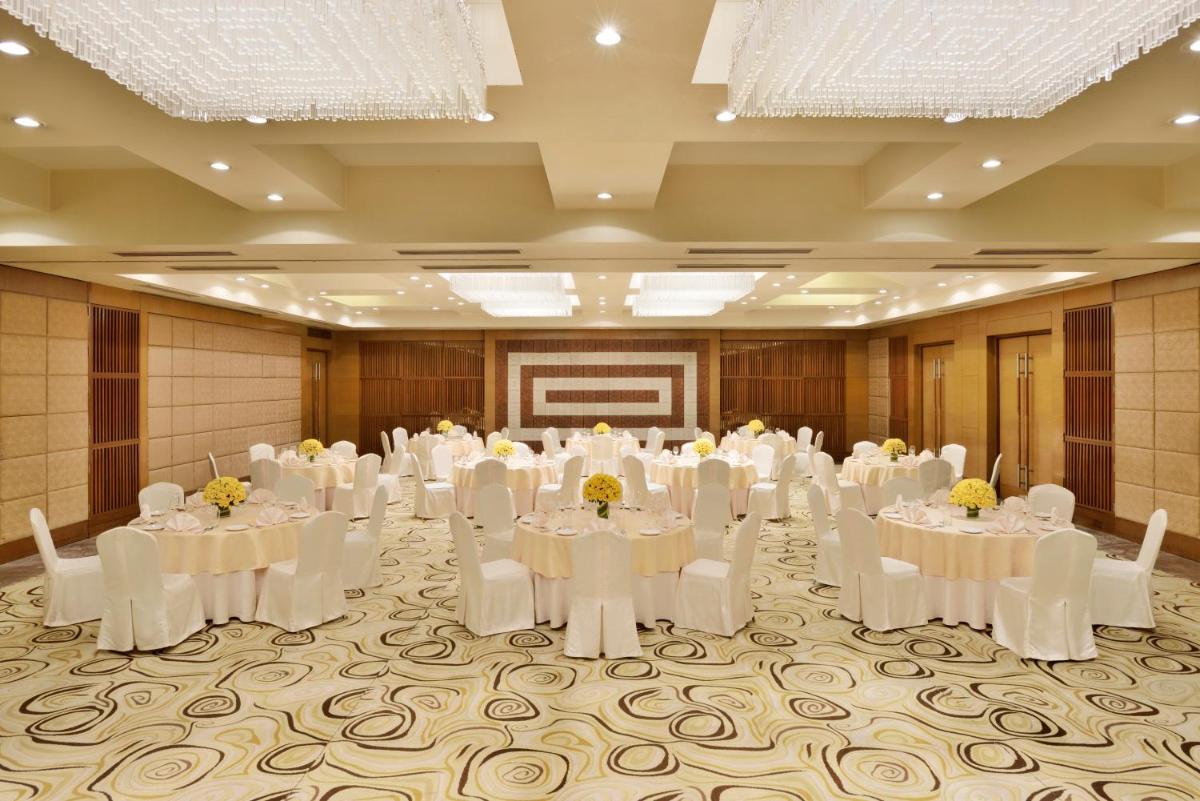 a banquet hall with white tables and chairs and a screen at Radisson Blu Hotel, Indore in Indore