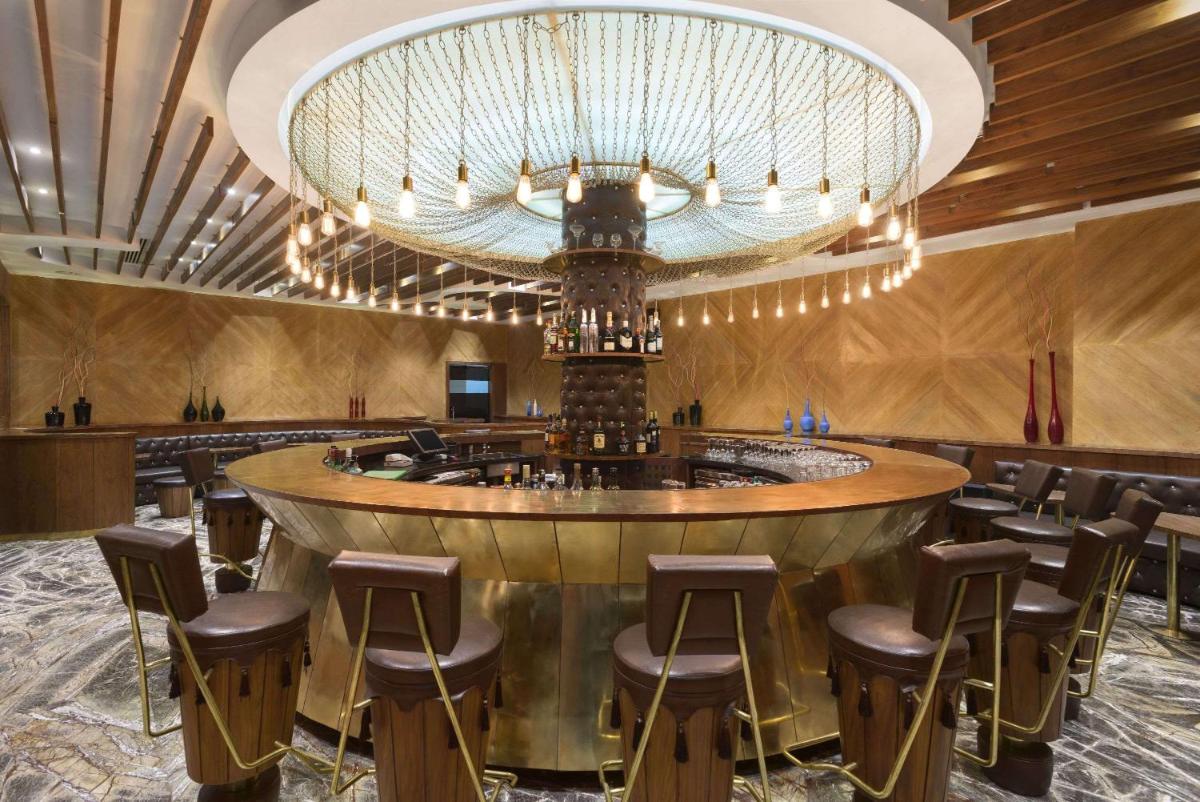 a bar in a restaurant with a large chandelier at Saura Hotel, Agra - A Club Mahindra Associate in Agra