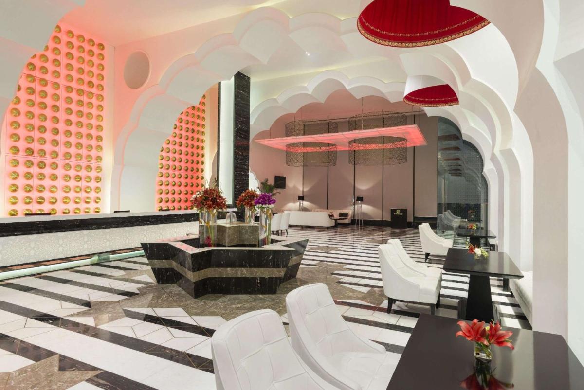 a lobby with white chairs and tables in a building at Saura Hotel, Agra - A Club Mahindra Associate in Agra