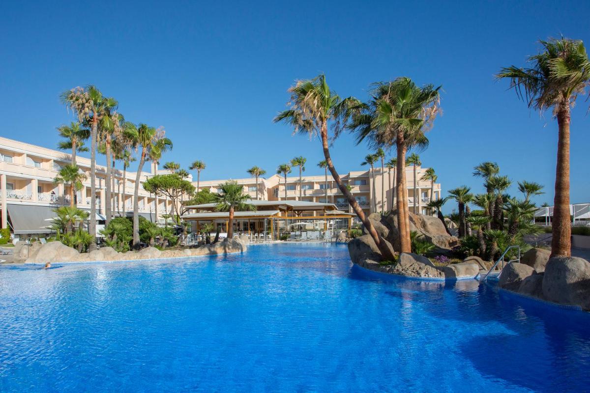 Una gran piscina con palmeras en un complejo turístico. en Hipotels Playa La Barrosa - Adults Only, en Chiclana de la Frontera