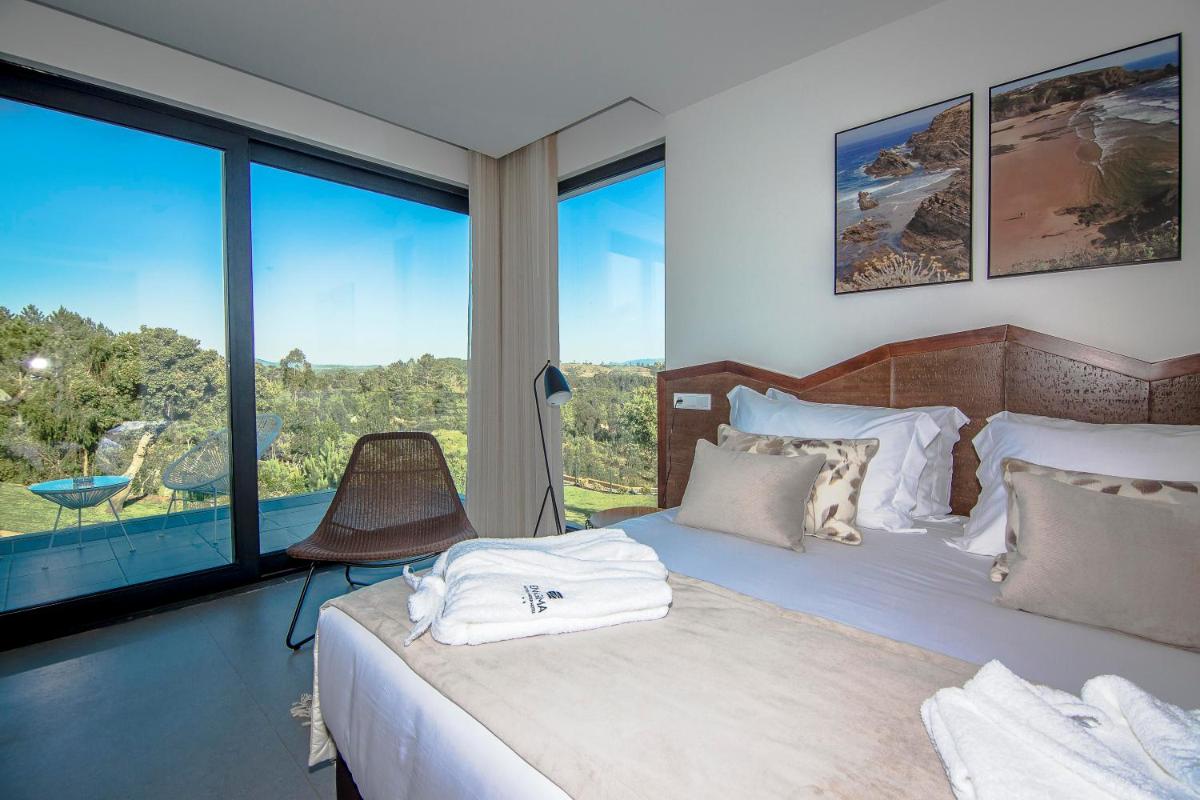 um quarto com uma cama e uma janela grande em Enigma - Nature & Water Hotel em São Teotónio