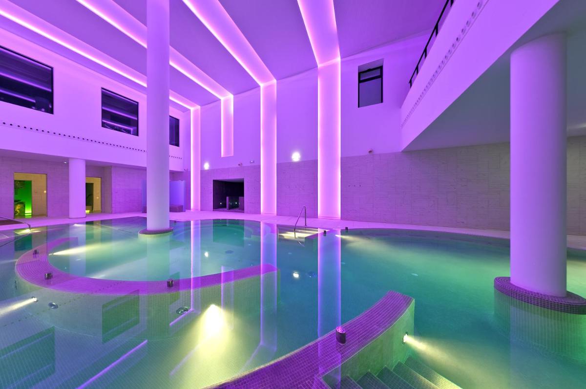 una piscina cubierta en un edificio con iluminación púrpura en URH Hotel Spa Zen Balagares, en Overo