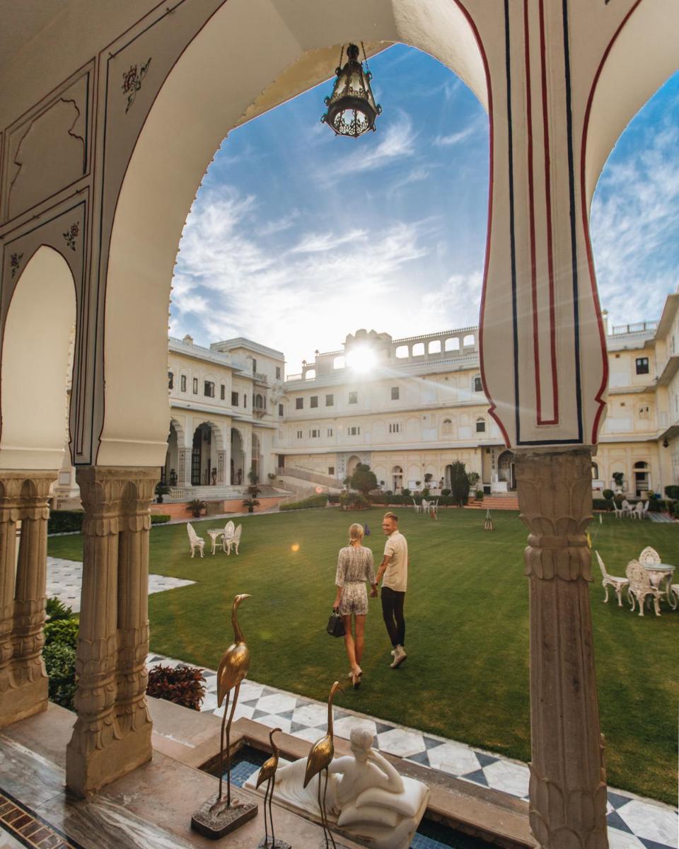 two people walking in the courtyard of a building with birds at The Raj Palace (Small Luxury Hotels of the World) in Jaipur