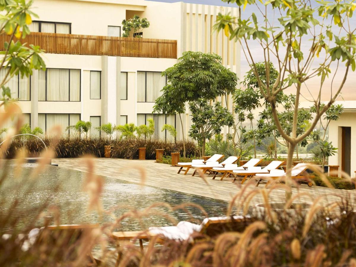 a hotel with a pool and lounge chairs in front of a building at Hyatt Hyderabad Gachibowli in Hyderabad