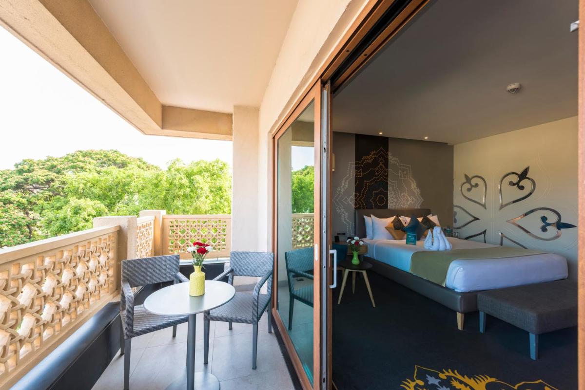 a bedroom with a bed and a balcony with a table and chairs at Grand Mercure Mysore - An Accor Brand in Mysore