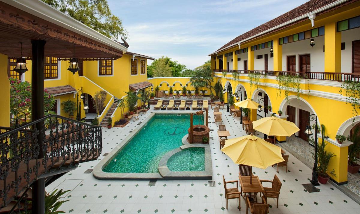 an outdoor pool with tables and umbrellas next to a building at Forte Kochi in Cochin