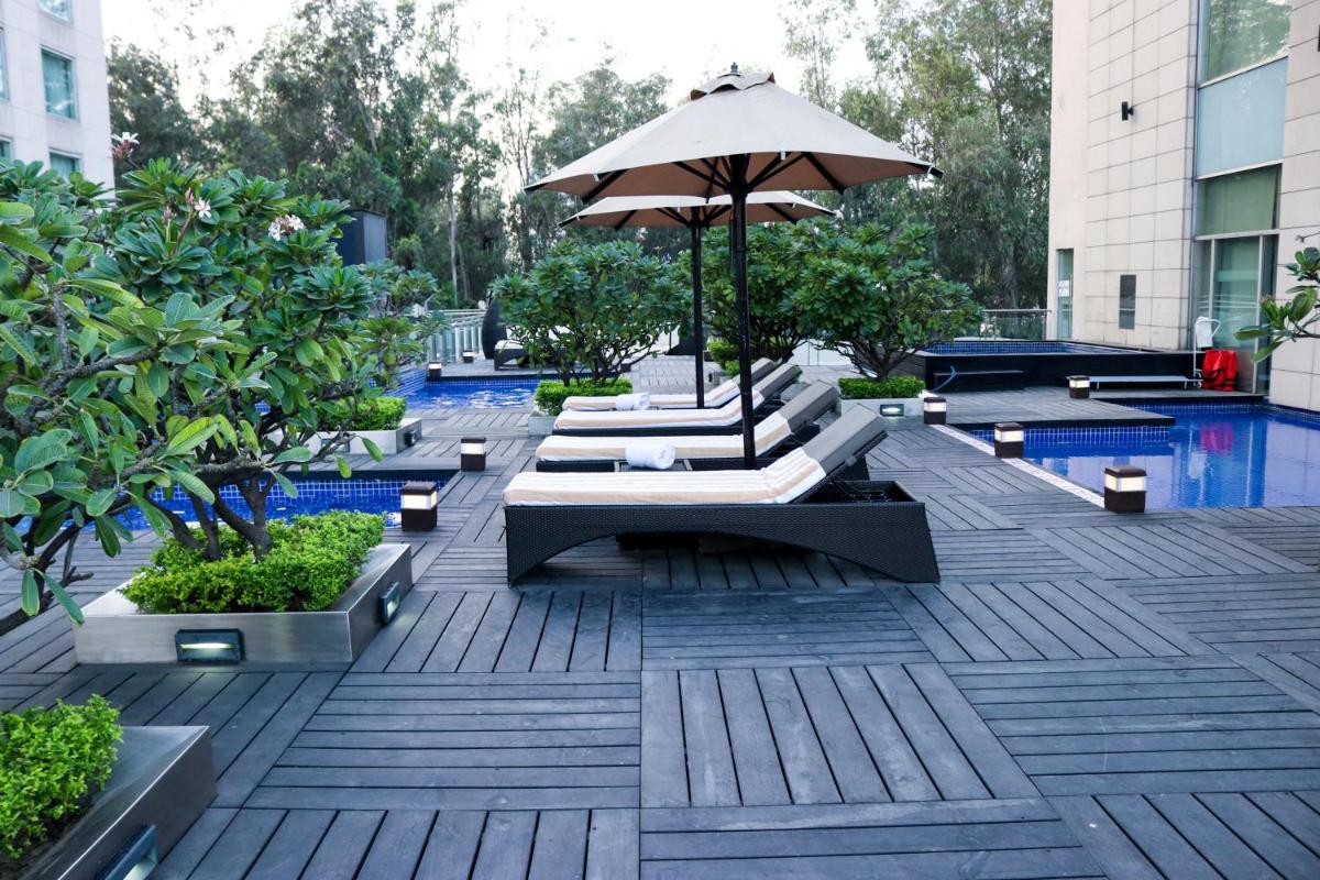 a patio with an umbrella and benches and a pool at Radisson Blu Hotel, Greater Noida in Greater Noida