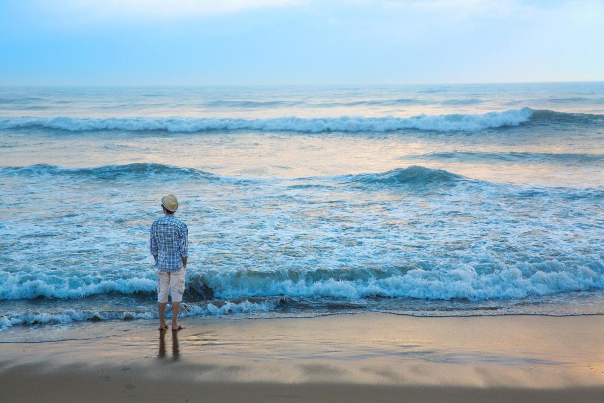 a man standing on the beach looking at the ocean at Novotel Chennai Chamiers Road in Chennai