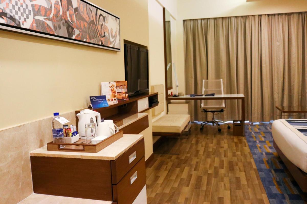 a hotel room with a bed and a desk with a television at Radisson Blu Hotel, Greater Noida in Greater Noida