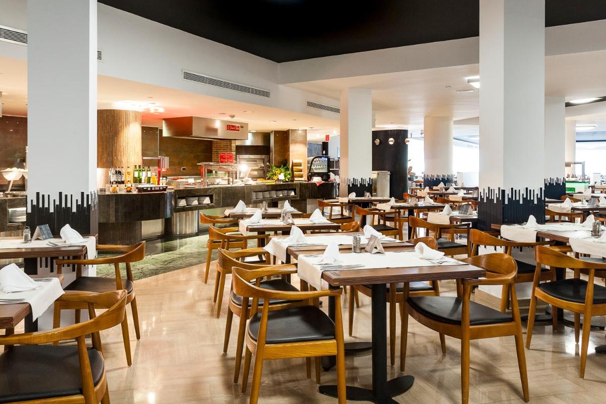 Un restaurante con mesas y sillas de madera y una cocina. en Sandos Monaco - Adults Only, en Benidorm