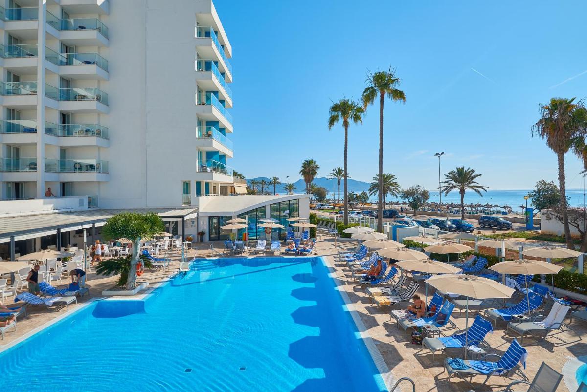 Una imagen de la piscina del resort con sillas y sombrillas. en Hipotels Hipocampo - Adults Only, en Cala Millor