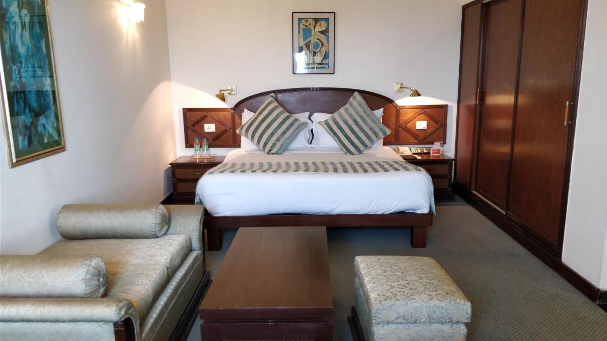 a hotel room with a bed and a couch at The Suryaa New Delhi in New Delhi a hotel room with a bed and a couch at The Suryaa New Delhi in New Delhi