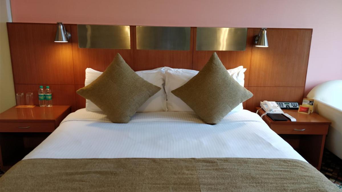 a bed in a hotel room with pillows on it at The Suryaa New Delhi in New Delhi a bed in a hotel room with pillows on it at The Suryaa New Delhi in New Delhi