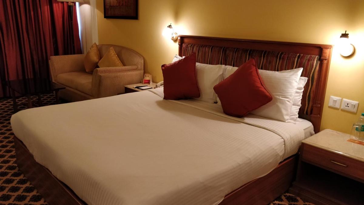 a hotel room with a large bed and a chair at The Suryaa New Delhi in New Delhi a hotel room with a large bed and a chair at The Suryaa New Delhi in New Delhi