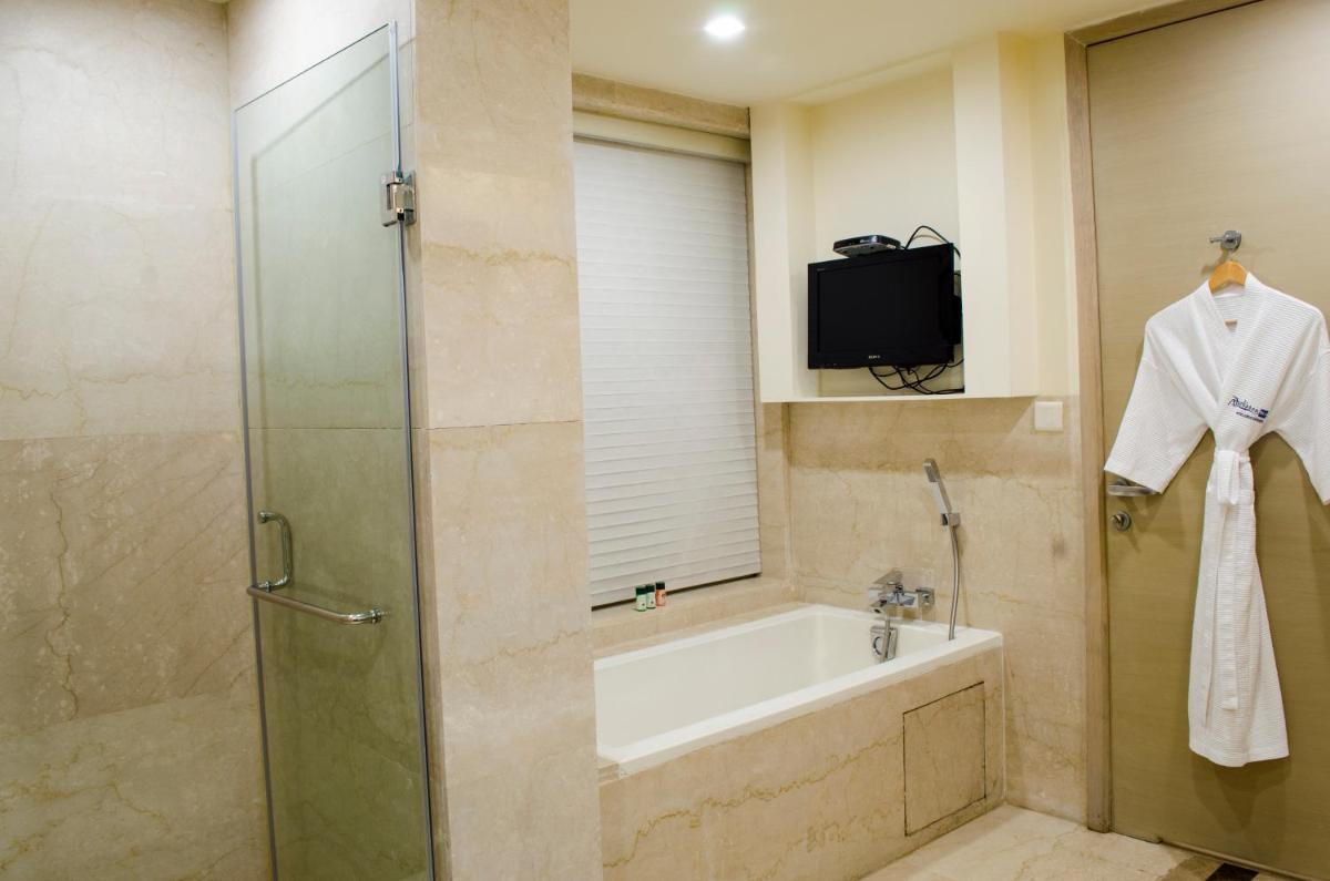 a bathroom with a shower and a tub and a television at Radisson Blu Hotel, Greater Noida in Greater Noida