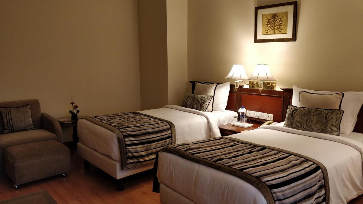 a hotel room with two beds and a chair at Jaypee Vasant Continental in New Delhi