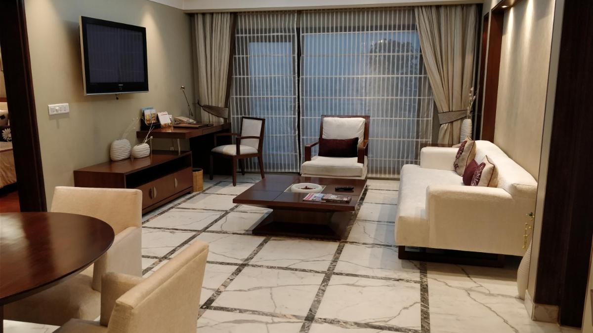 a living room with chairs and a table and a tv at Jaypee Vasant Continental in New Delhi