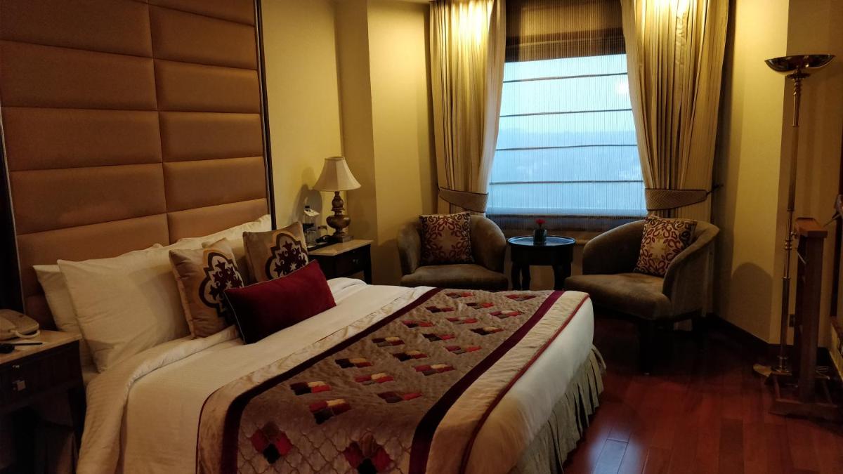 a bedroom with a bed and two chairs and a window at Jaypee Vasant Continental in New Delhi
